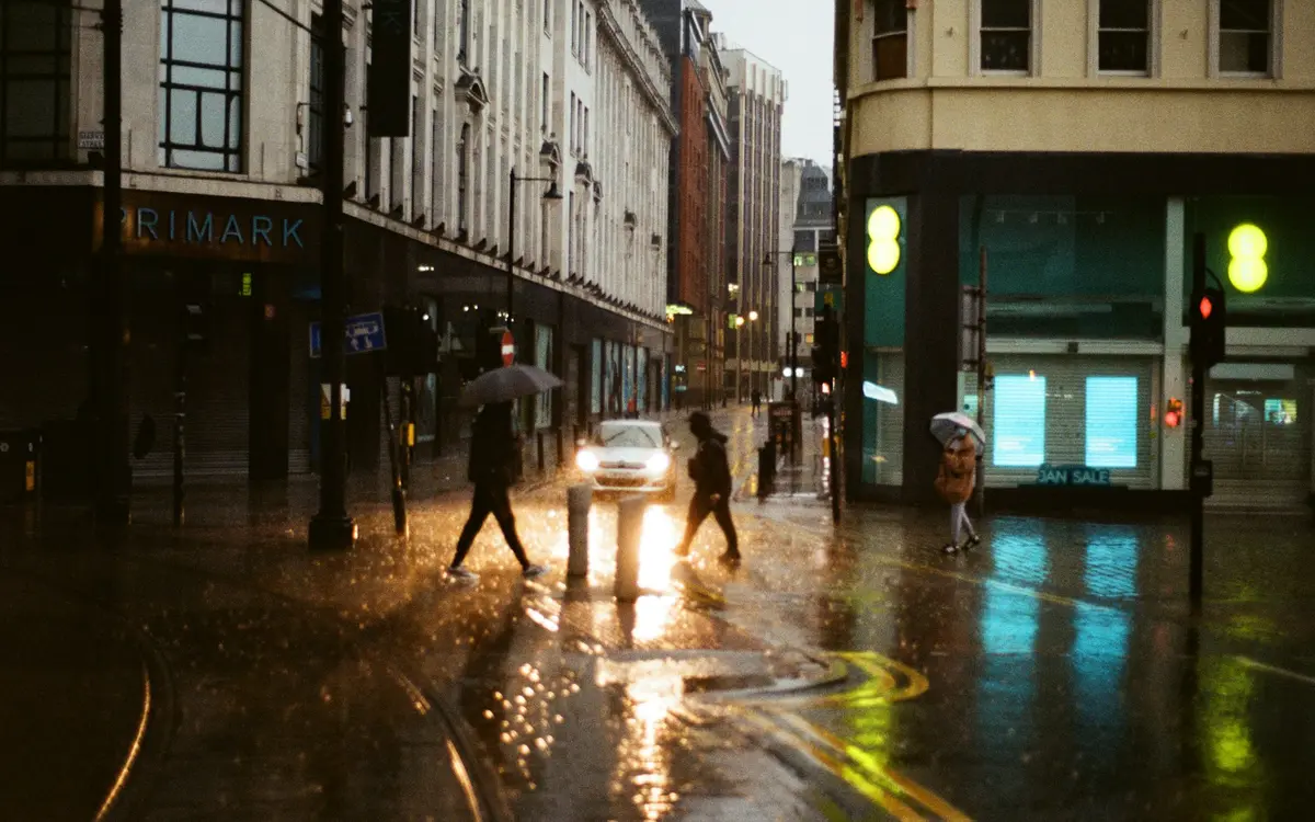 People with umbrellas crossing a wet Manchester street