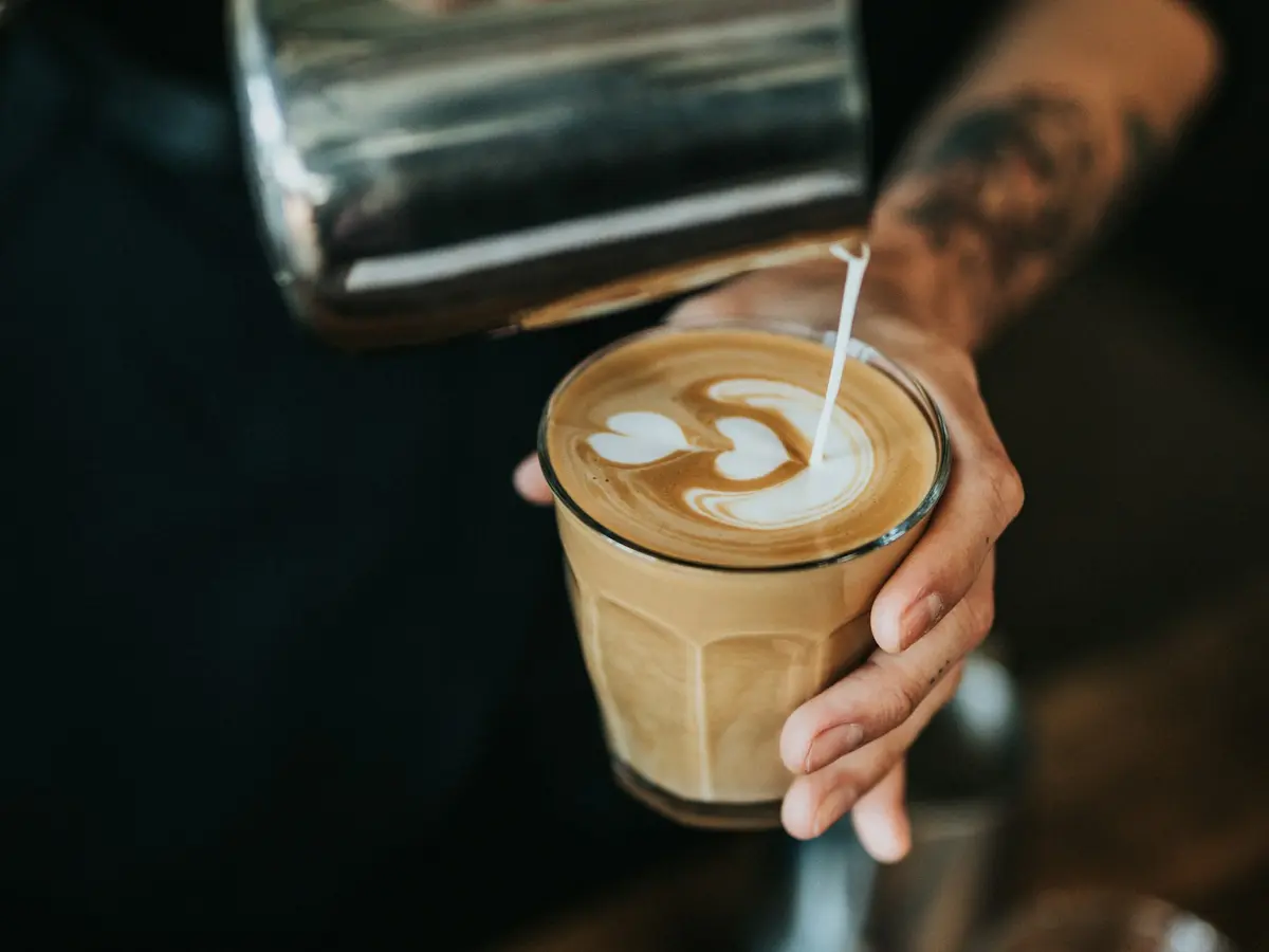 A barista pouring latte art into a glass